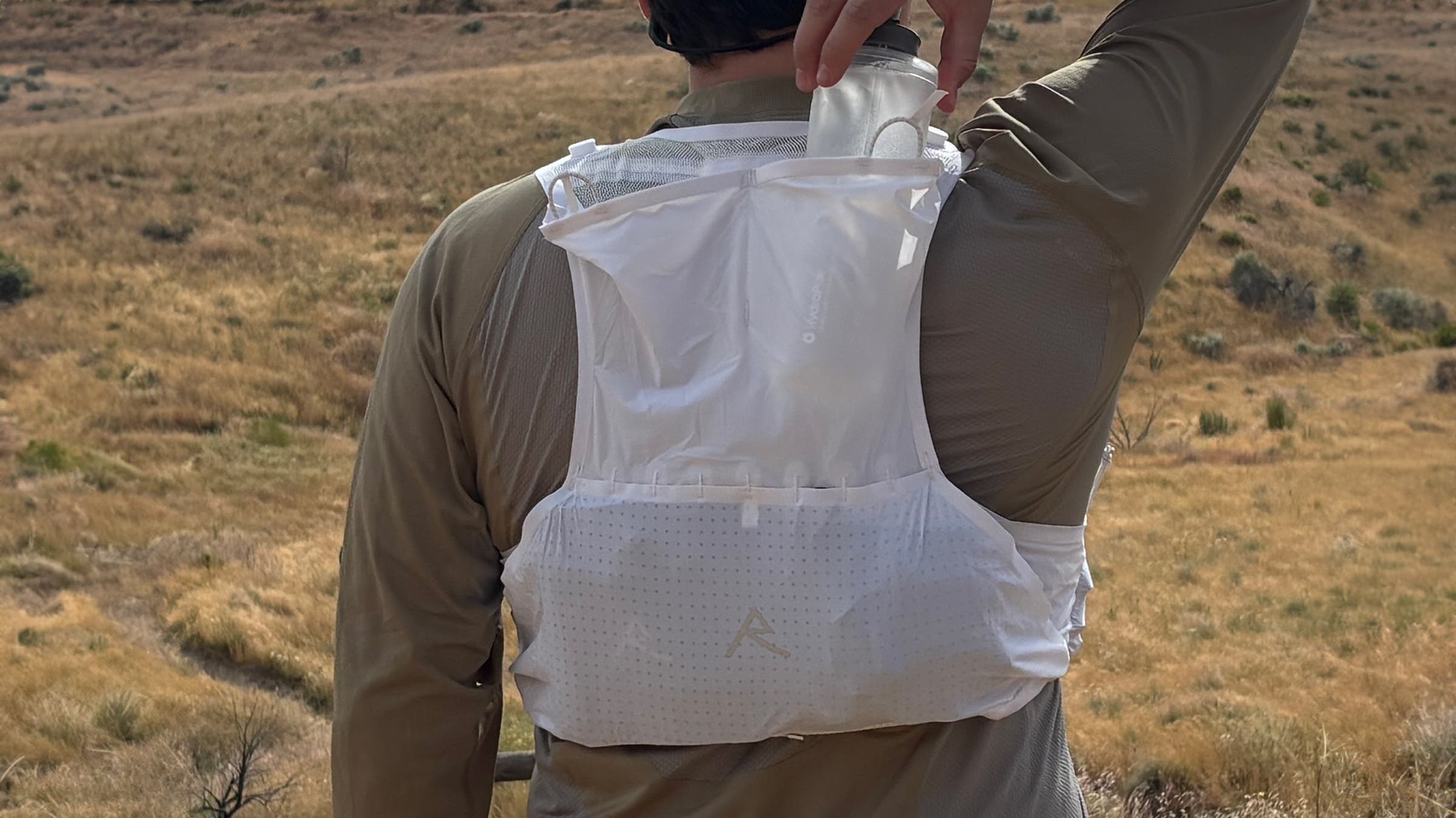 Close up of tester Will Porter wearing Raide LF 5L running vest showing off back pocket with soft water bottle being pulled out